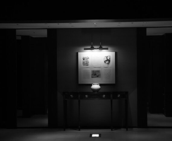 Indrammet kunsttryk over et mørkt konsolbord med en lille keramikvase i en entré